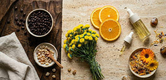 Flat lay of five Island Natural Skincare hero ingredients: blue tansy flowers, frankincense resin, coffee beans, orange slices, and calendula blooms on a warm linen surface