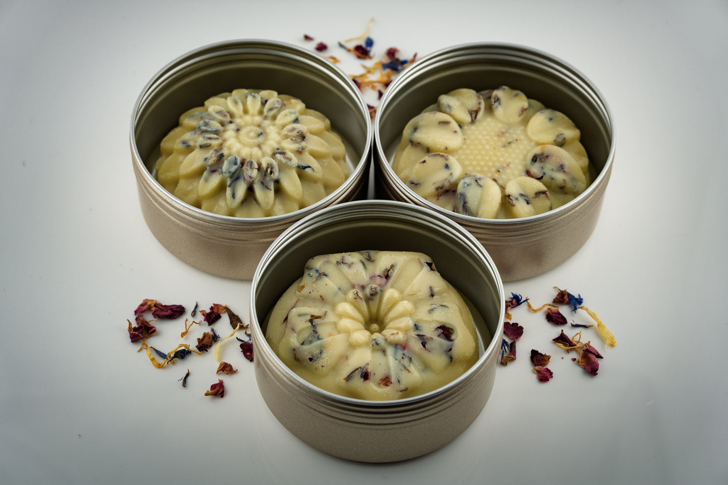 Three floral shaped botanical scented tallow lotion bars decorated with dried flowers made by Island Natural Skincare on a light gray background