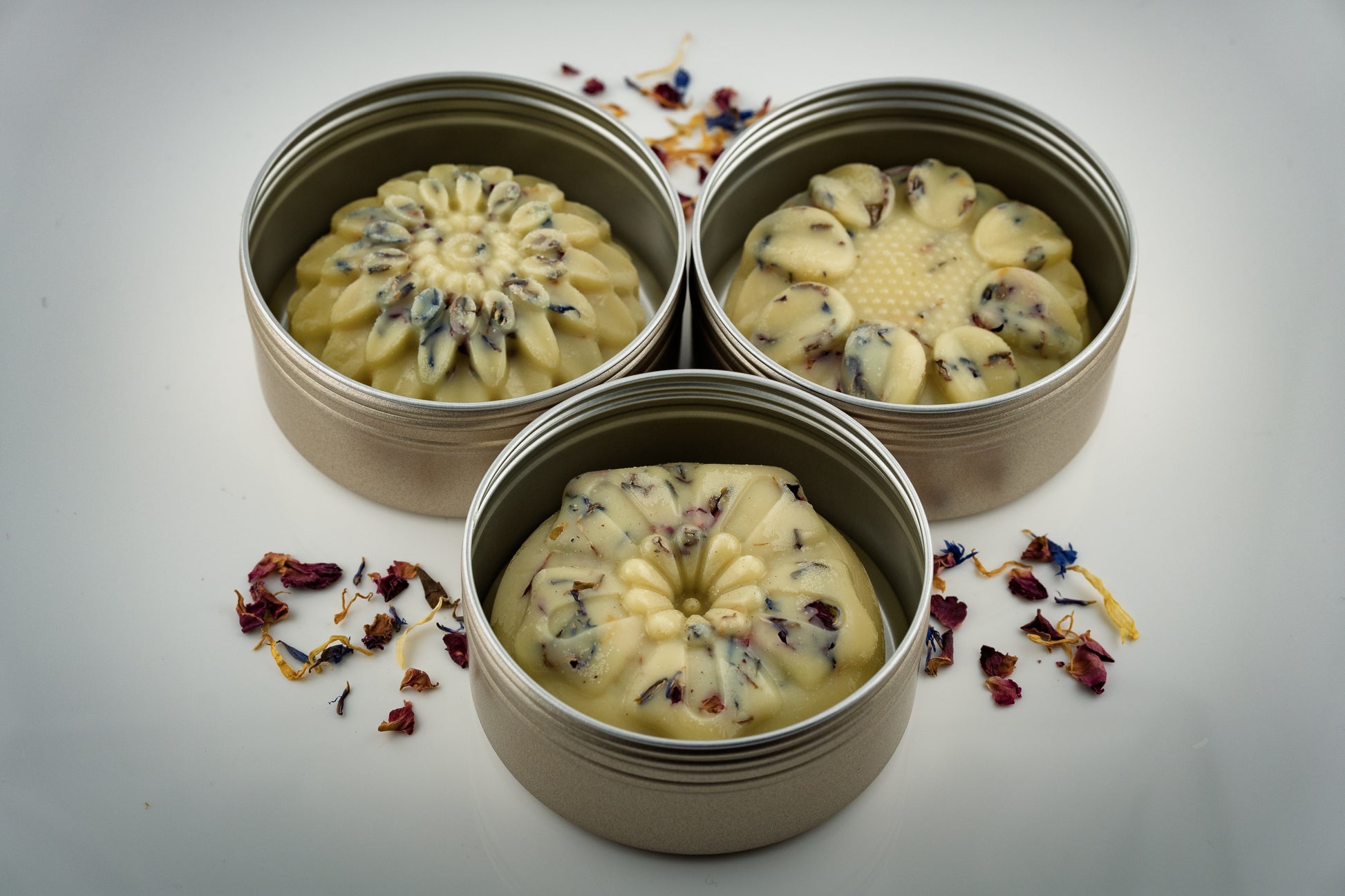 Three floral shaped botanical scented tallow lotion bars decorated with dried flowers made by Island Natural Skincare on a light gray background