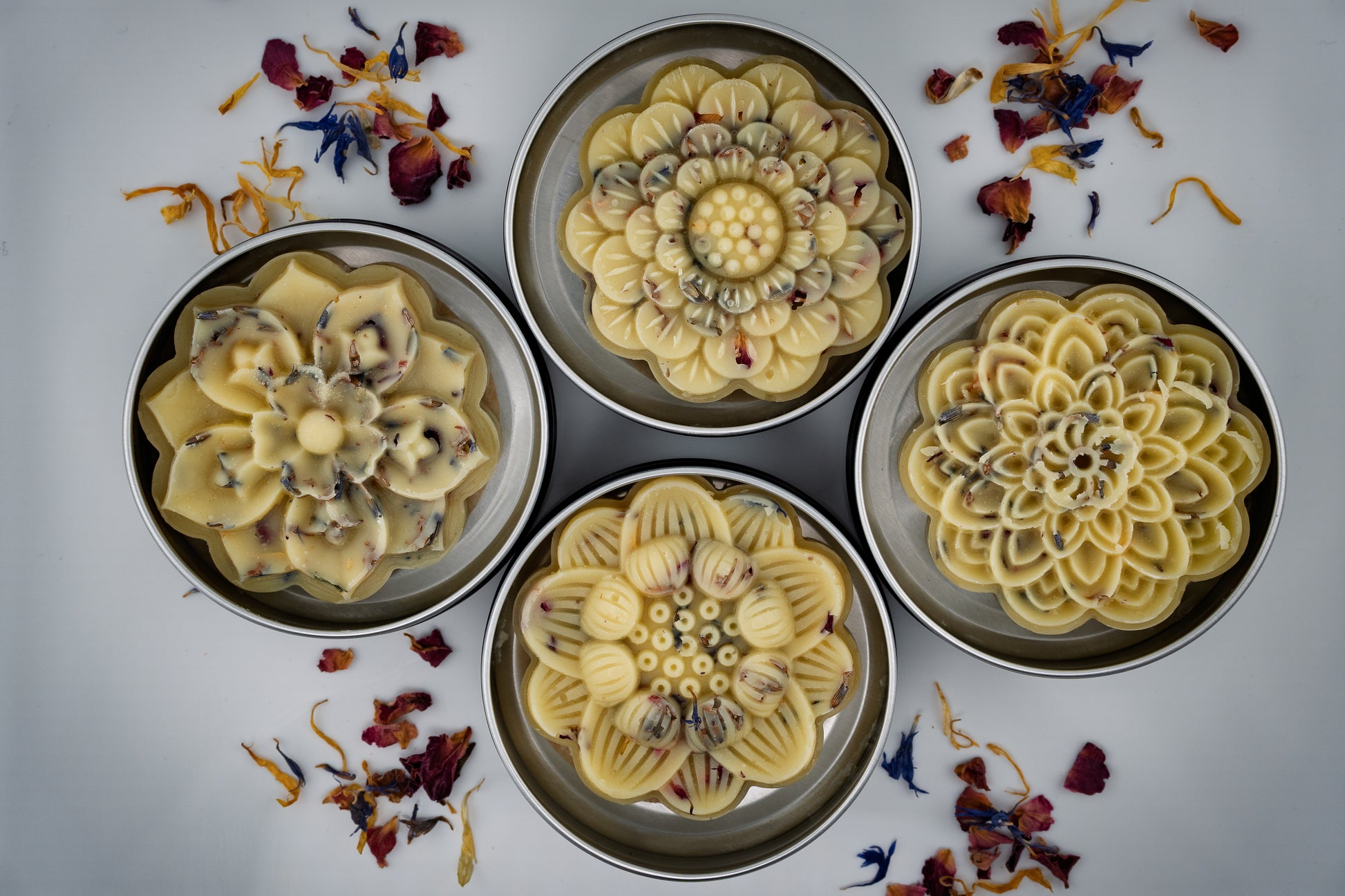 Four decorative flower-shaped tallow lotion bars on a white background with dried flowers made by Island Natural Skincare