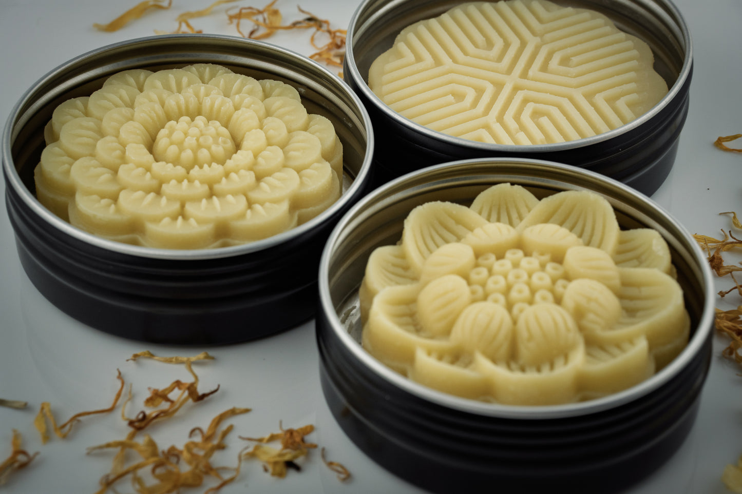 Three round containers with floral-patterned Island Natural Skincare lotion bars on a white surface.