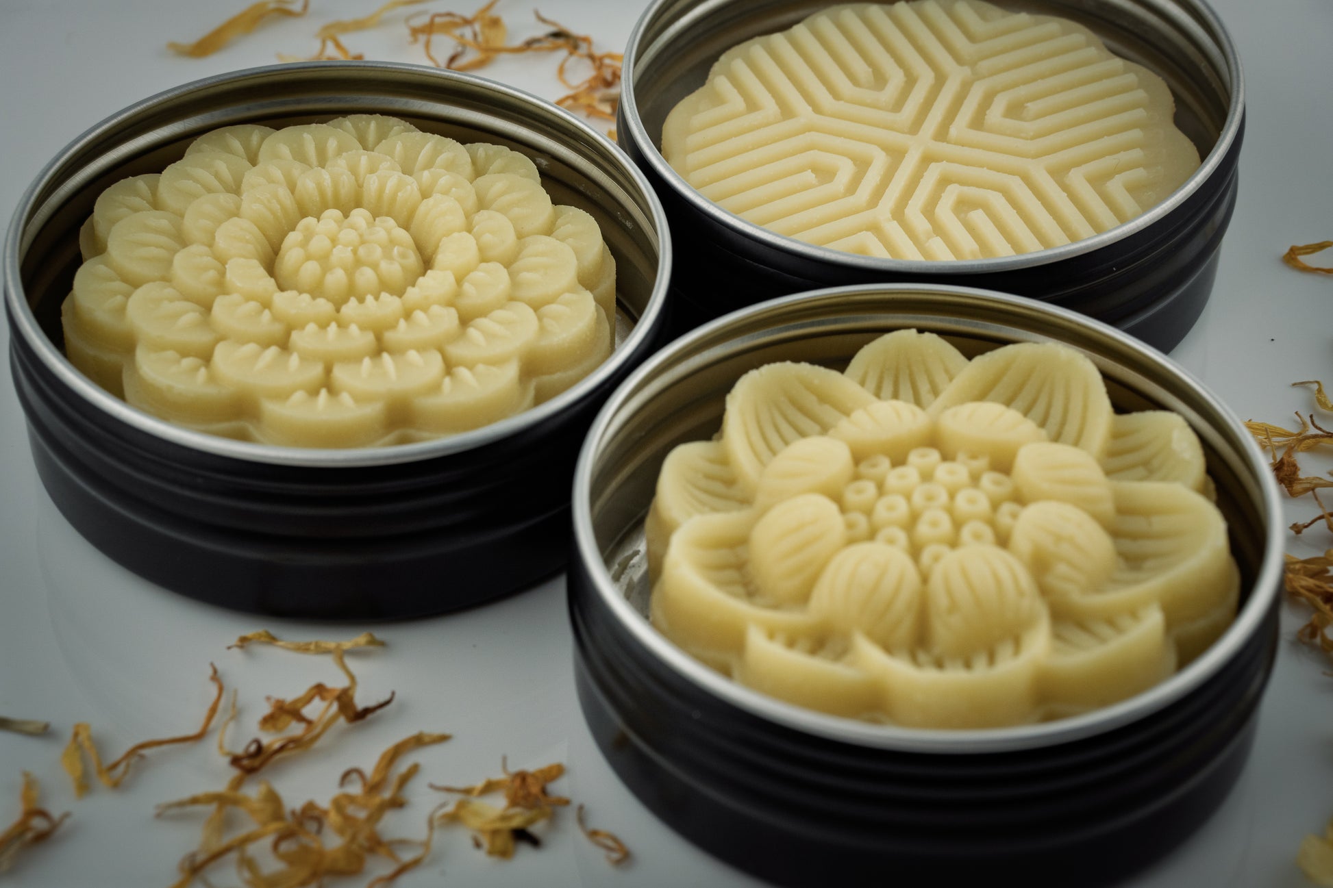 Three round containers with floral-patterned Island Natural Skincare lotion bars on a white surface.