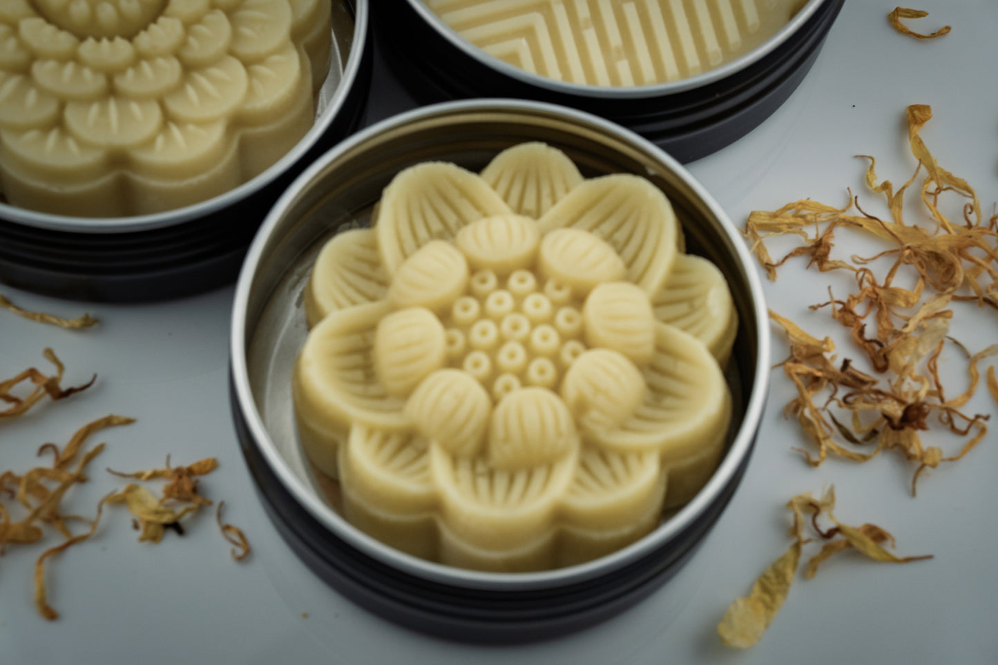 Decorative Island Natural Skincare lotion bars shaped like flowers in a tin with dried flowers on the side.