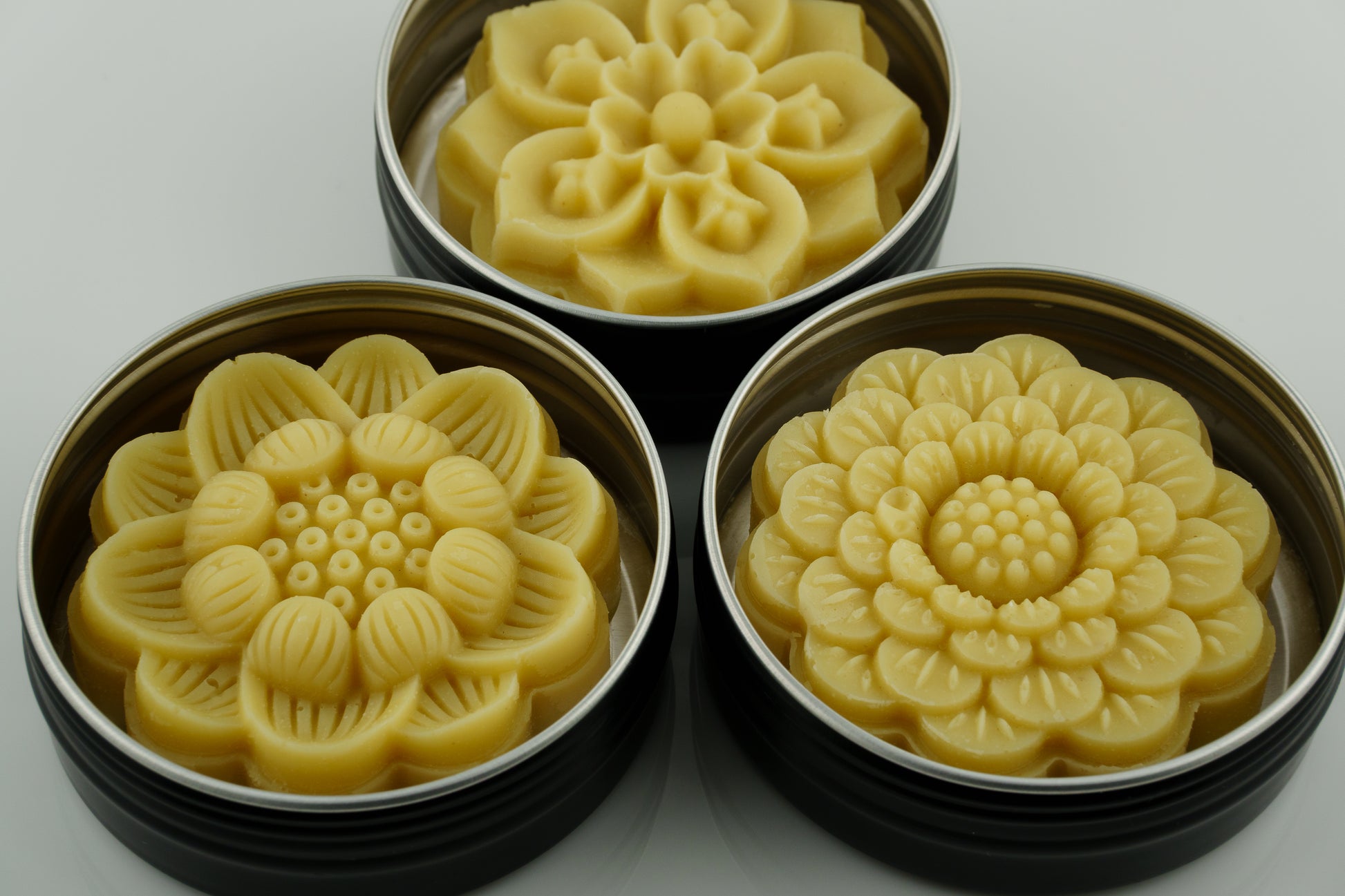 Three metal tins with floral-shaped orange tallow lotion bars on a white background
